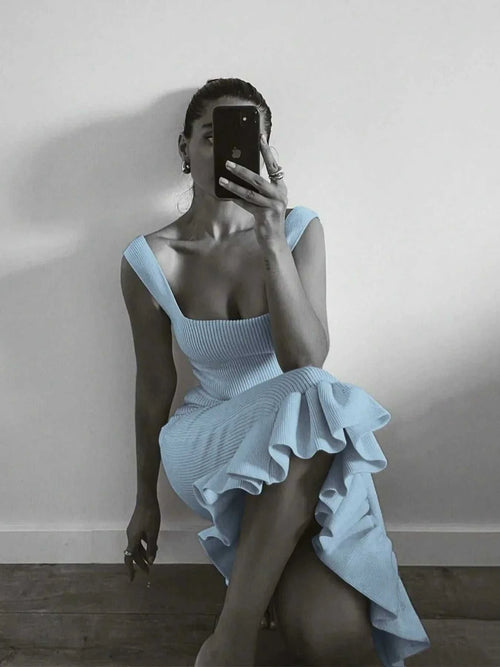 Woman wearing a light blue ribbed knit bodycon dress with ruffle hem sitting against a wall taking a mirror selfie