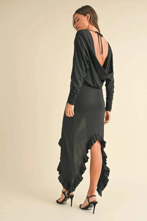 Woman wearing black Mable Backless Asymmetric Ruffle Hem Dress with deep back and ruffled hem, paired with black heels