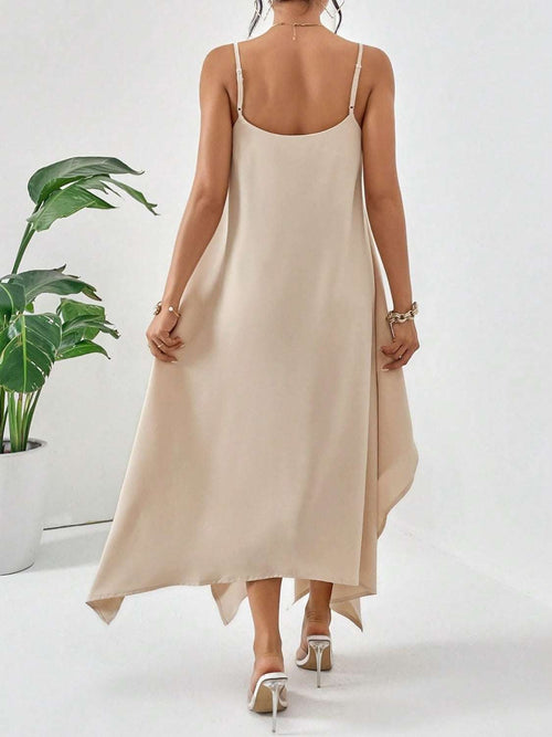Back view of a woman wearing a beige scoop neck midi cami dress with thin straps and asymmetrical hem, paired with white heels.