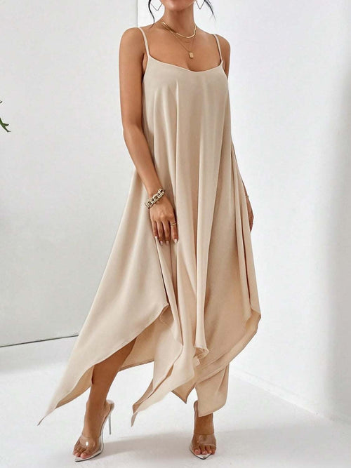 Beige scoop neck midi cami dress with flowy asymmetrical hem and spaghetti straps worn with clear high heel sandals.