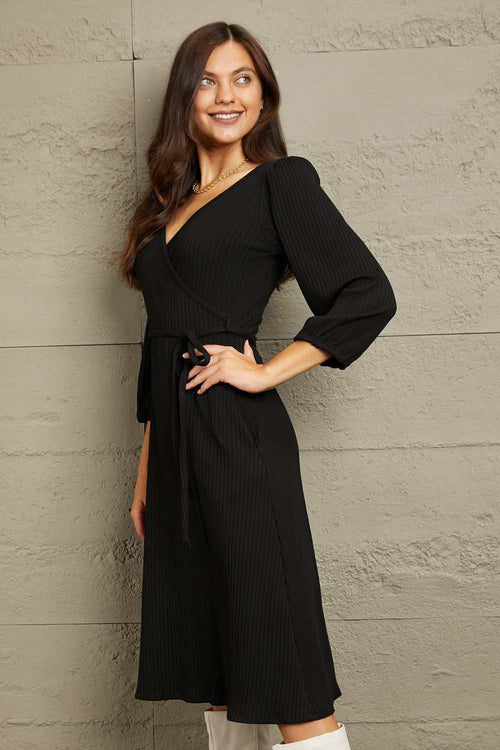 Woman wearing Culture Code Full Size black surplice flare midi dress with ruched long sleeves and waist tie