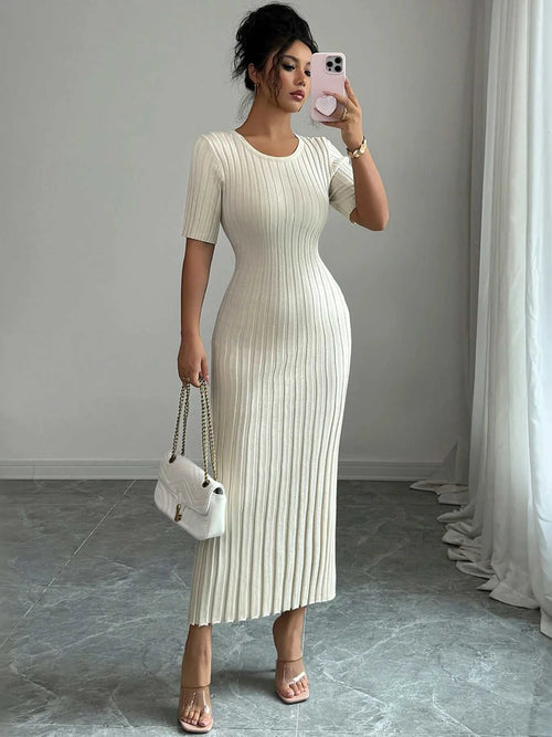Woman wearing a ribbed round neck short sleeve white sweater dress with moderate stretch, holding a white handbag and taking a mirror selfie