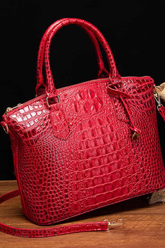 Red PU leather handbag with crocodile texture and shoulder strap on wooden surface