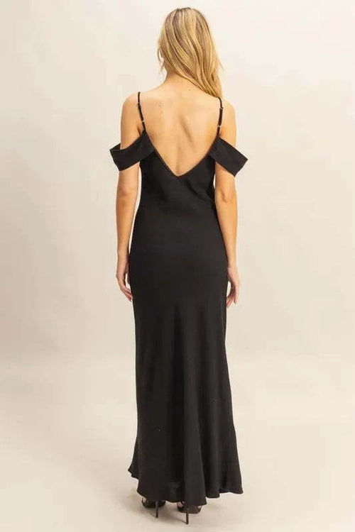Rear view of a woman wearing a black HYFVE Flattering Fit Cami Maxi Dress with an asymmetrical ruffled design and low back, showcasing its sleek, maxi-length silhouette.