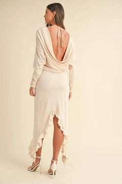 Woman wearing a cream backless asymmetric ruffle hem dress with long sleeves and high heels