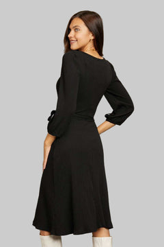 Woman wearing a black Culture Code Full Size surplice flare ruching midi dress with long sleeves and waist tie viewed from the back