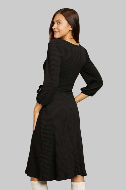 Woman wearing a black Culture Code Full Size surplice flare ruching midi dress with long sleeves and waist tie viewed from the back