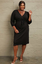 Culture Code Full Size black surplice flare midi dress with ruching sleeves and waist tie detail worn by plus-size model