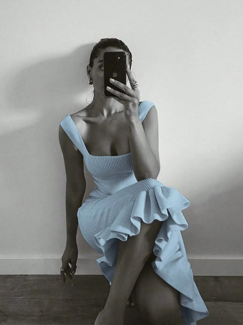 Woman wearing a light blue ribbed knit bodycon dress with ruffle hem sitting against a wall taking a mirror selfie