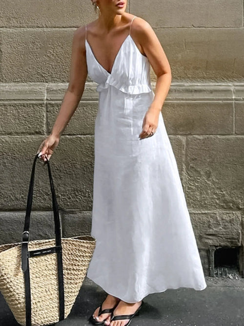 Woman wearing white ruffled V-neck maxi dress with thin straps carrying a large woven tote bag