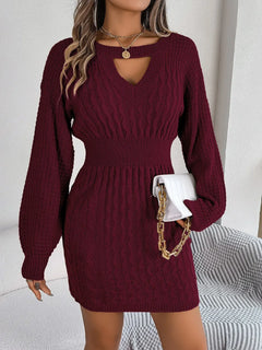 Woman wearing a burgundy cable-knit cutout round neck slit sweater dress with long sleeves and a fitted waist holding a white purse with gold chain strap