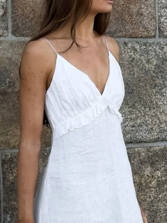 woman wearing white ruffled v-neck maxi dress with thin straps against stone wall background
