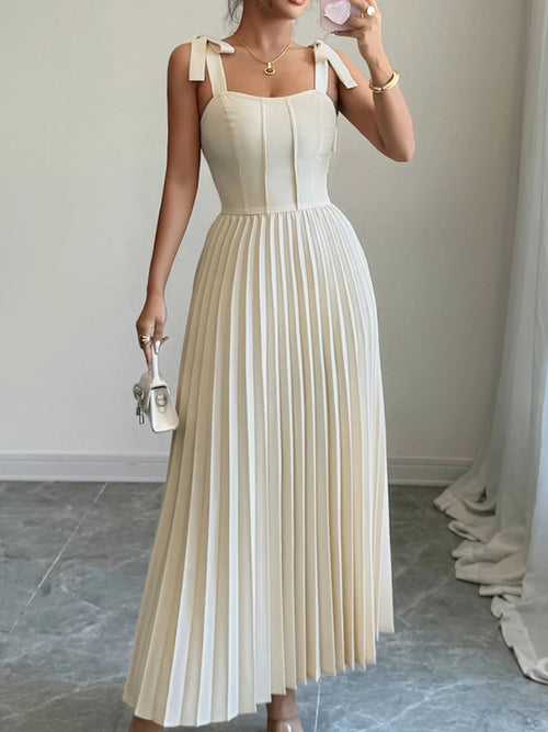 Woman wearing a cream pleated tie-shoulder maxi dress with bow details carrying a small white handbag