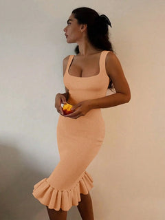 Woman wearing peach ribbed knit bodycon dress with ruffle hem holding orange fruit