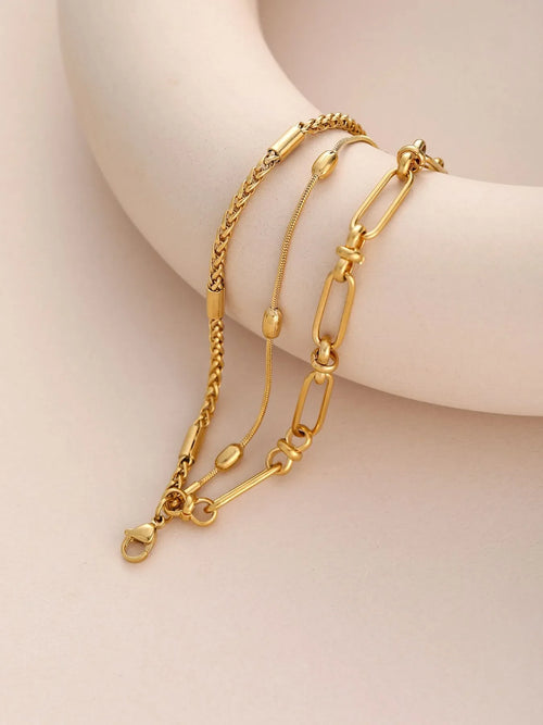 18K gold-plated layered chain necklace and bracelet set on a beige background