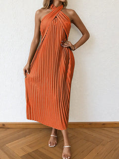 Woman wearing an orange pleated halter neck midi dress with crisscross ties and no stretch, styled with sandals on wooden floor.