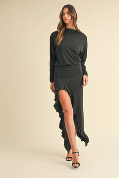 Woman wearing a black Mable Backless Asymmetric Ruffle Hem Dress with a high slit and ruffle detail, paired with black heels.