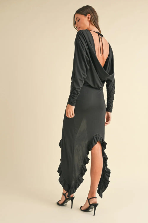 Woman wearing black Mable Backless Asymmetric Ruffle Hem Dress with deep back and ruffled hem, paired with black heels
