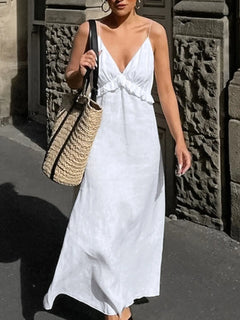 Woman wearing white ruffled V-neck maxi dress carrying straw bag on city street