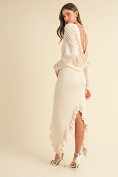 Woman wearing a beige backless asymmetric ruffle hem dress with long sleeves and high heels