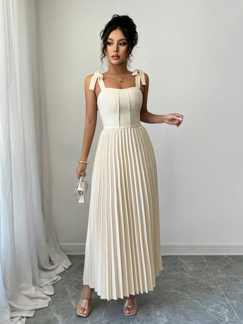 Woman wearing elegant cream pleated tie-shoulder maxi dress with bow details and square neckline