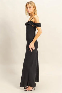 Woman wearing a black HYFVE Flattering Fit Cami Maxi Dress with asymmetrical ruffled neckline and slim fit silhouette.