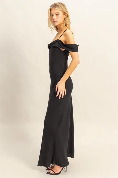 Woman wearing a black HYFVE Flattering Fit Cami Maxi Dress with asymmetrical ruffled neckline and slim fit silhouette.