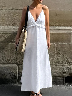 Woman wearing white ruffled V-neck maxi dress with thin straps and carrying woven tote bag