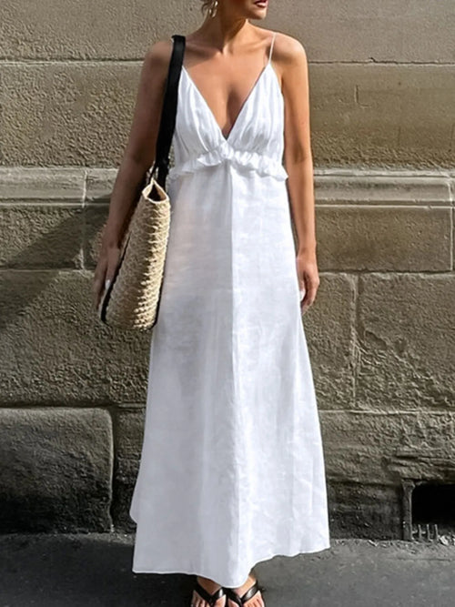 Woman wearing white ruffled V-neck maxi dress with thin straps and carrying woven tote bag