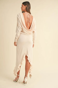 Woman wearing a cream backless asymmetric ruffle hem dress with long sleeves and high heels