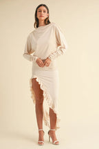Model wearing beige backless asymmetric ruffle hem dress with long sleeves and high slit.