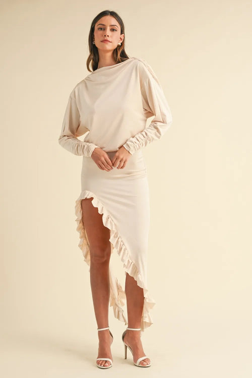 Model wearing beige backless asymmetric ruffle hem dress with long sleeves and high slit.
